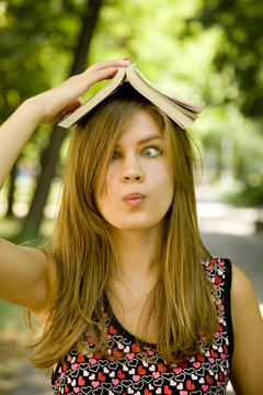 Blonde girl with book over head at the park.