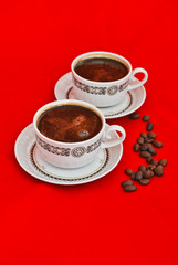 Two cups of coffee and coffee beans isolated on red