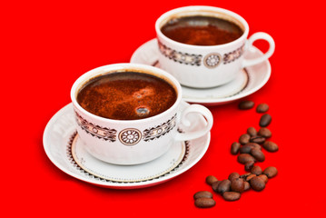 Two cups of coffee and coffee beans isolated on red