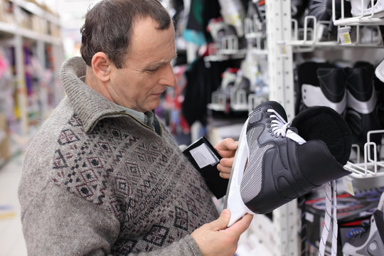 elderly man in gray sweater chooses skates in big sports shop