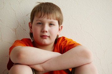 Boy sits with his back to the wall, putting his folded arms