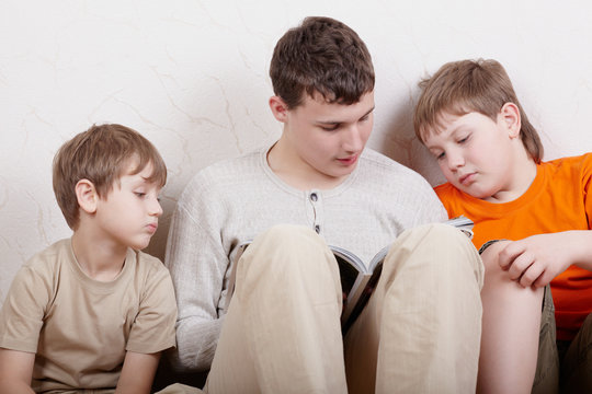 Three boys sit side by side with their backs to wall and read
