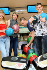 Obraz premium Two girls and youths stand near tenpin bowling with balls