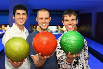Friends stand alongside and in hands hold balls for bowling
