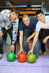 Fototapeta premium Three men bent over to heave up balls for bowling