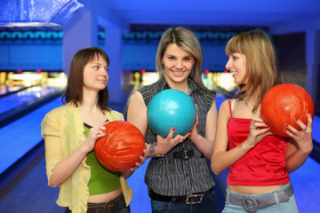 Three girlfriends hold balls for bowling and look on each other