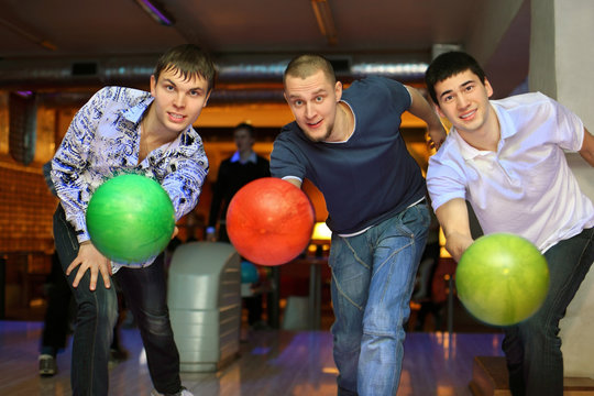 Three fellows throw balls on lane in bowling club