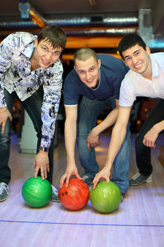 Three men bent over to heave up balls for bowling