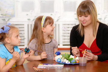 Young woman with children paints an Easter egg