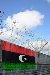 Barbwire and grey wall with Libya national flag