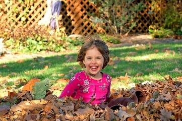 Young girl jumps into a pile of autumn leaves