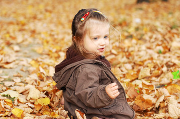 Adorable baby girl plays in autumn forest in a pile of leaves