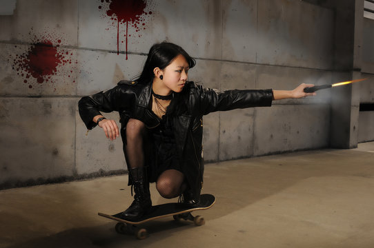 Young asian gang member shooting a gun while riding a skateboard