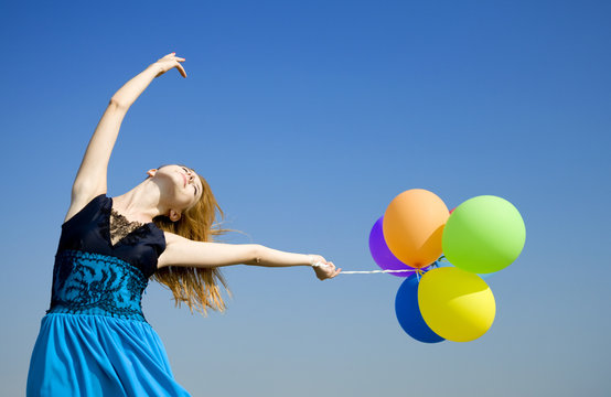 Redhead girl with colour balloons at blue sky background.