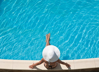 Fototapeta na wymiar Young woman sitting on the ledge of the pool.