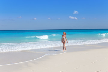 Fototapeta na wymiar The young woman goes on a beach at sea edge