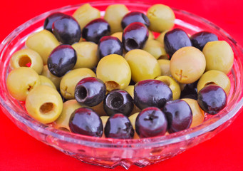 Black and green olives in a crystal bowl isolated on red