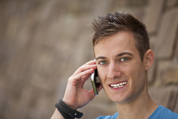 l&auml;chelnder junger Mann an einer Mauer mit Smartphone