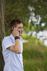 junger Mann steht am Flussufer und telefoniert mit Smartphone