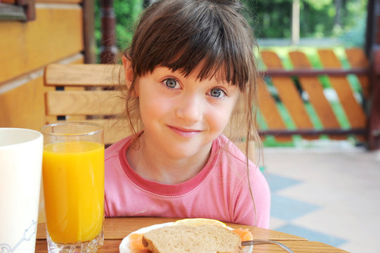 Smiling child girl has a healthy breakfast outdoors