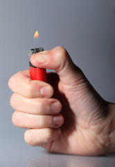 Hand igniting red cigarette lighter
