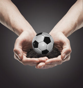 A handful soil with classic soccer ball in the man's hands