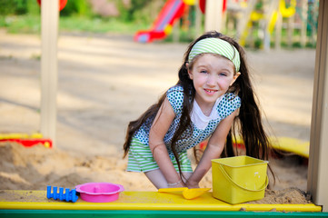 Happy child girl wearing green headband plays in a sandbox