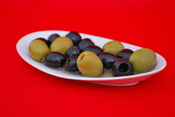 Black and green olives in a plate on a red background
