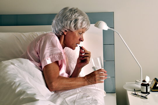 Ältere Frau nimmt  eine Tablette im Bett
