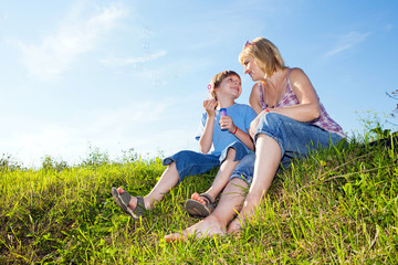 Fototapeta premium Boy and mother with soap bubbles against a sky
