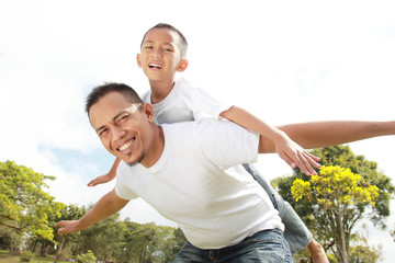 father giving his son piggyback ride outdoors against sky