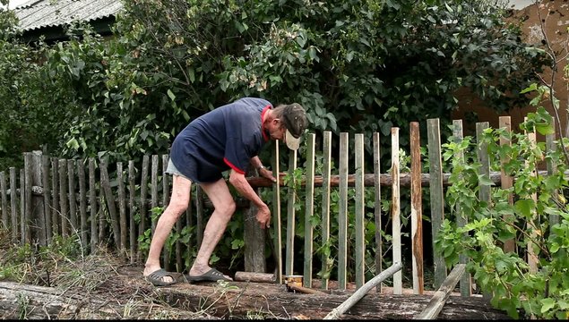 Пожилой мужчина ремонтирует забор.