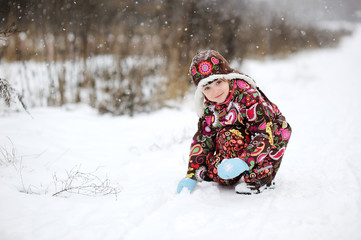 Child girl in colorful snowsiut plays outdoors in snowfall