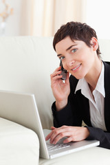Cute Businesswoman lying on a sofa with a laptop and a phone