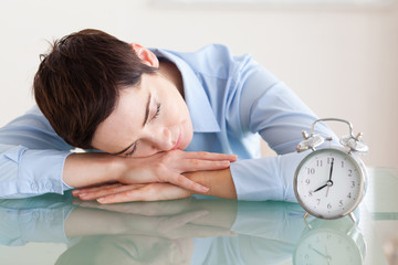 Sleeping woman with her head on the desk next to an alarmclock