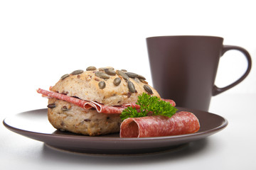 Kürbiskernbrötchen mit Salami und Tasse Kaffee
