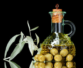 olive oil in jar and olives on black background