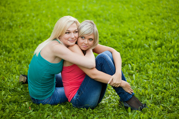 Fototapeta premium Two girls sitting on the grass, embracing