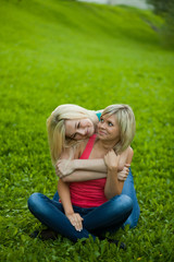 Two girls sitting on the grass, embracing