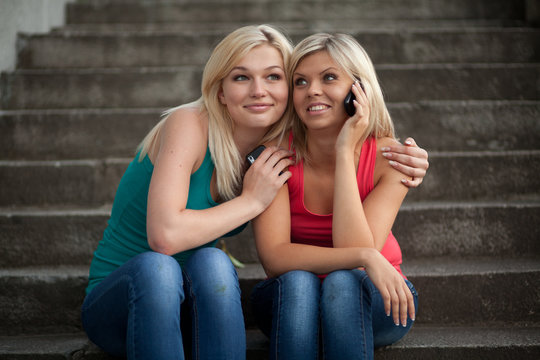 Two girls sitting on the steps with the phones and talk to fun