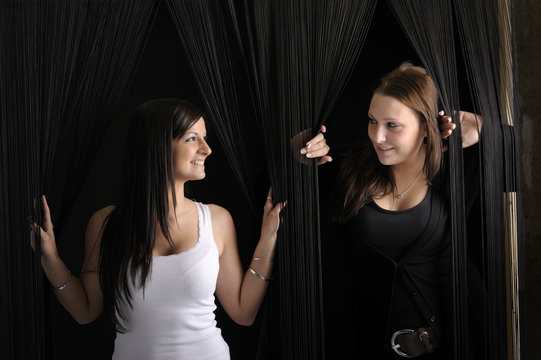 two young women looking from behind a cord curtain