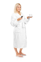 Young woman in bathrobe holding a coffee cup and mobile phone