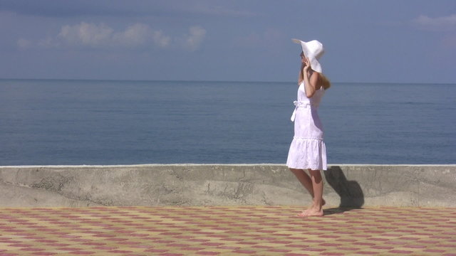 Woman with white hat walk and looks at sea