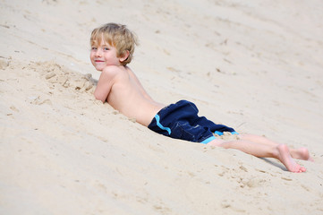 Boy laying in the sand at the base of a sand dune