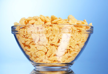 tasty cornflakes in glass bowl on blue background