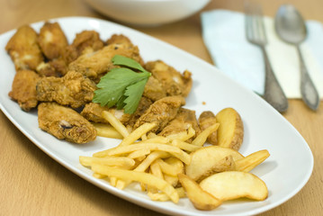 golden fried chicken and fried potatoes in a white plate
