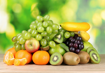 Ripe juicy fruits on wooden table on green background