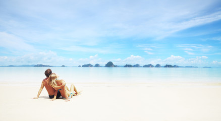 Fototapeta na wymiar Young couple sitting on the sand and looking to a blue tropical sky
