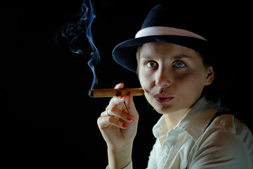 Obraz premium Woman in black hat with smoking cigar black background isolated