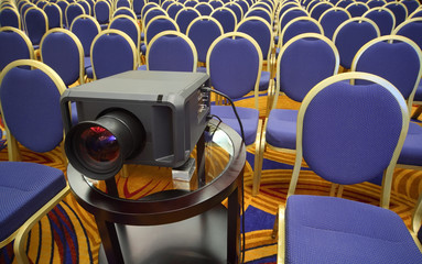Black projector on background of rows of yellow-blue chairs